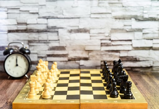 Chess pieces on chess board and alarm clock on wooden table. Blurred background with copy space photo