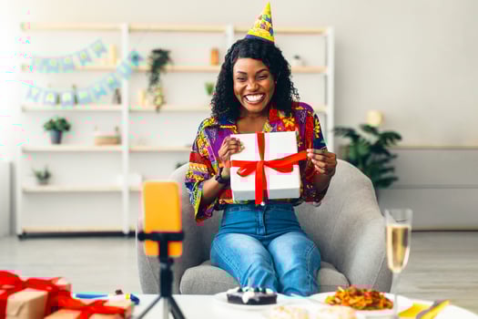 Happy Black Woman Showing Birthday Gift Box To Phone Celebrating Her Holiday Remotely Online Via Call With Distant Friends Sitting At Home. B-Day Present Delivery. Selective Focus photo