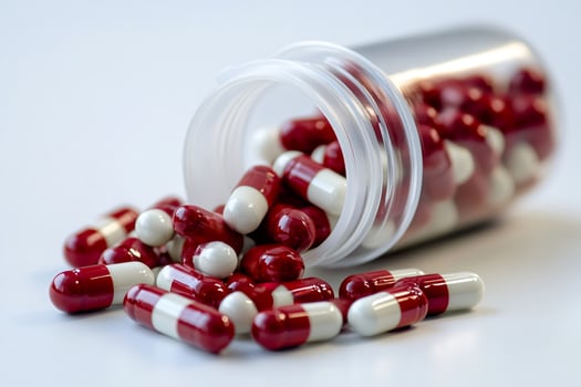 Red and white capsules spilling from a pill bottle on a white background photo