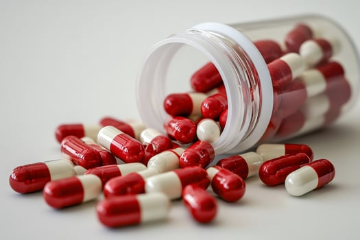 Red and white capsules spilling from a prescription bottle on a white surface photo