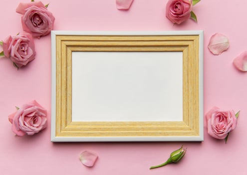Empty frame surrounded by pink roses and petals on pink background photo