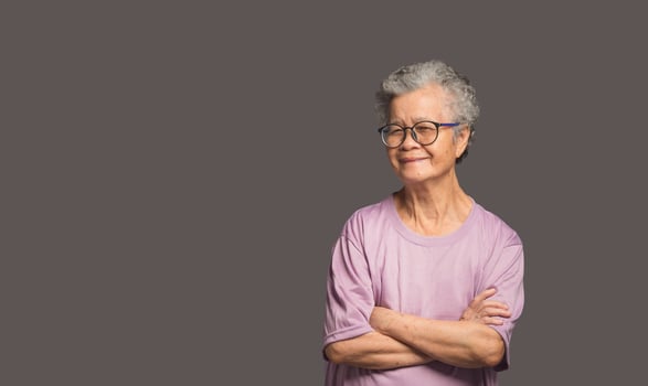 Elderly Asian woman looking at the camera with a smile while standing on a gray background photo
