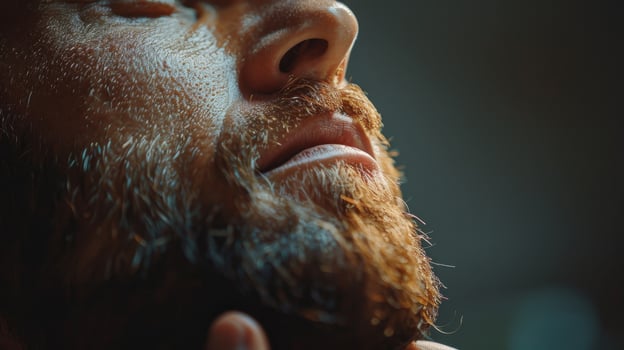 A man with a detailed beard rests with his eyes closed, basking in gentle light that highlights his facial features. He seems to be in a peaceful moment, possibly reflecting or meditating. photo