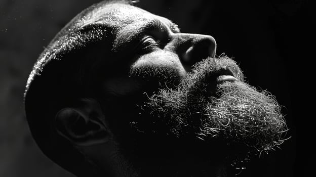 A man with a full beard tilts his head back, evoking a contemplative mood. The interplay of light and shadows creates a striking visual, highlighting facial features. photo