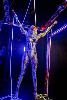 Blonde as a cyber robot. Girl in shining silver armor in neon. Blonde with fantastic makeup and image in dark key and colored light, posing in cyberspace. wires around hands, general plan photo