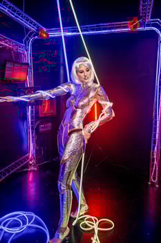 Blonde as a cyber robot. Girl in shining silver armor in neon. Blonde with fantastic makeup and image in dark key and colored light, posing in cyberspace. Around her hands and body wires, neon color photo