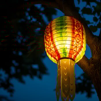 Colorful paper lantern hanging on tree branch glowing at dusk with deep blue sky traditional festival light photo