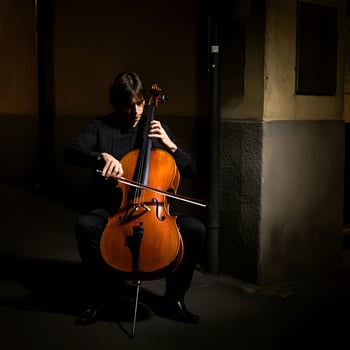 Young man playing cello at night with focused expression in moody urban street setting under soft lighting photo