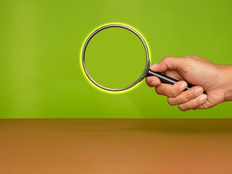 Close-up of hand holding a magnifying glass against a green background photo