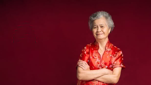 Senior woman wearing a traditional cheongsam qipao dress with a smile while standing arms crossed on a red background photo