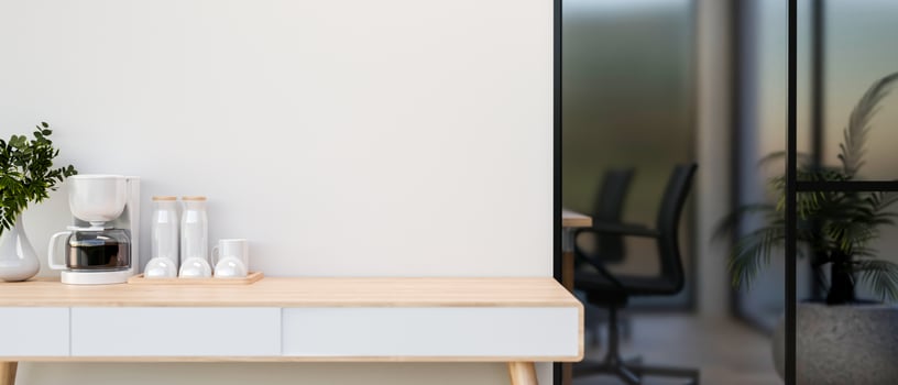 A coffee maker on the wooden table beside the white wall of company meeting room. photo