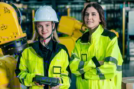 Women engineers pose with robotic equipment in a high-tech industrial setting during daytime photo