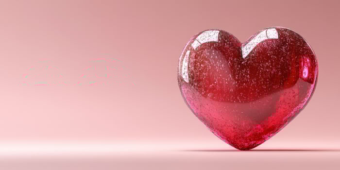 Decorative red heart made of glass resting on a soft pink background with sparkling details and smooth edges photo