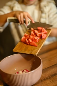 The girl cuts a tomato on a board and puts it in the salad bowl. She is focused, holding the knife carefully. photo