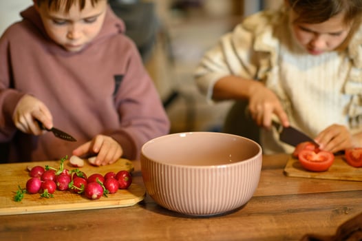 Children are cutting tomatoes and radishes into a salad bowl. They are focused, carefully holding the knives and working together. photo