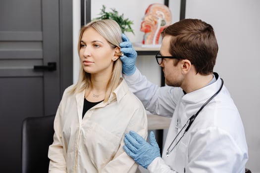 Otolaryngologist doctor checking young woman's ear using otoscope or auriscope at ENT clinic. Hearing exam photo