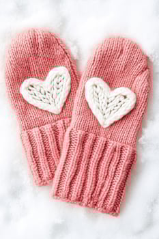 Knitted pink mittens with white heart decoration lying on soft snow in a winter setting evoking warmth and coziness photo