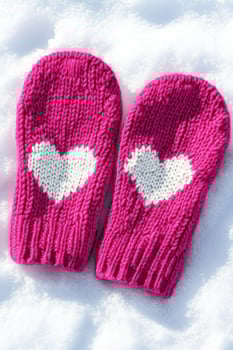 Knitted pink mittens with a white heart detail resting on soft snow in a cozy winter setting photo