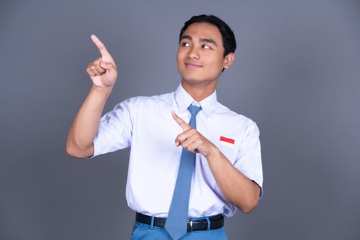 Indonesian Male High School Student in Uniform Smiling While Pointing Finger Isolated Background photo