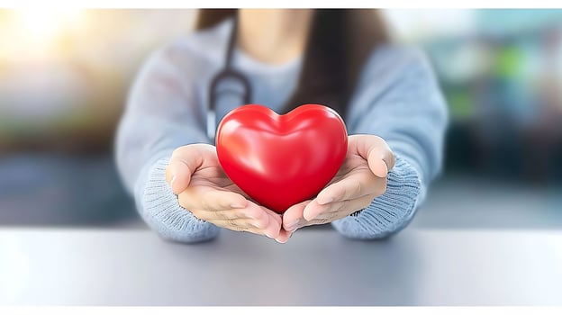 A healthcare professional presenting a red heart symbol in a caring gesture, with a blurred background photo