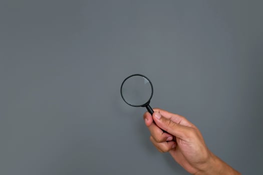 Man's hand holding a magnifying glass with copy space on a gray background photo