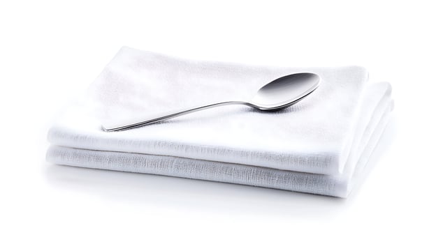 A polished silver spoon resting on neatly folded white napkins, creating a clean dining setting photo