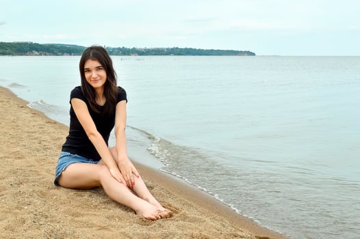 Attractive brunette girl sitting near water on a cloudy summer day. Lake Khanka, Russia. photo