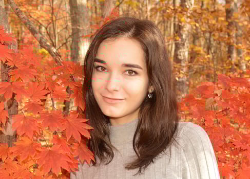 Young Russian pretty girl in gray sweater smiling and looking at the camera on autumn background with red maple leaves on a sunny warm day of October photo