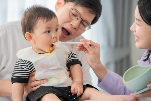 Father and mother feeding baby at home during meal time in a bright, cozy kitchen setting photo