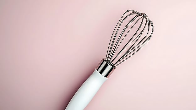 Close-up of a stainless steel whisk on a soft pink background, ideal for culinary-related designs photo