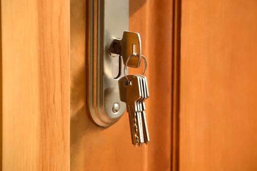 Metal key from the bunch of keys inserted into the lock of the wooden door. Warm colors, close up photo