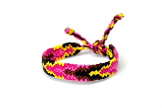 tied pink woven DIY friendship bracelet handmade of embroidery bright thread with knots isolated on white background photo
