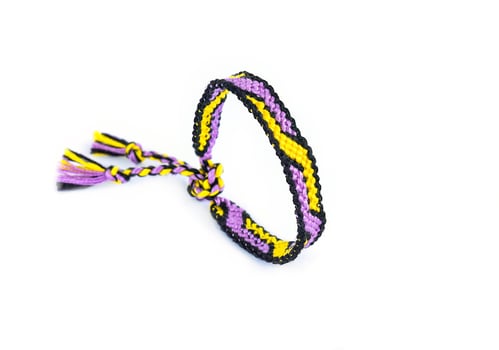 Lilac yellow woven DIY friendship bracelet handmade of embroidery bright thread with knots isolated on white background photo