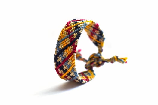 beige woven DIY friendship bracelet handmade of embroidery bright thread with knots isolated on white background photo