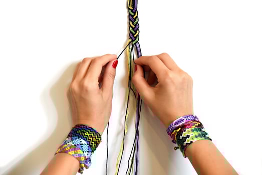 Female hands weaving a knot for DIY friendship bracelet Pigtail. Many handmade bracelets on girls wrists. Friendship bracelet making process, step by step. White background with copy space photo