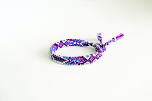 purple tied woven DIY friendship bracelet handmade of embroidery bright thread with knots isolated on white background photo