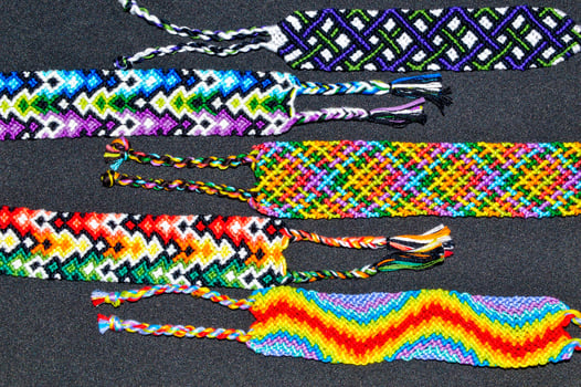 Selective focus of woven DIY friendship bracelets handmade of embroidery bright thread with knots on black background. photo