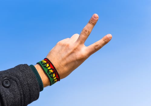 Handmade DIY friendship bracelet with Rasta flag pattern with a peace symbol on male wrist on sky background. photo