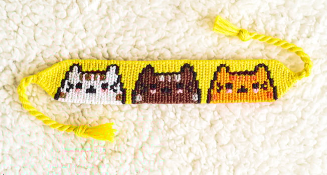 Woven DIY friendship bracelet with Cats pattern handmade of embroidery floss on blue background photo