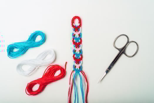 Unfinished woven DIY friendship bracelet next to scissors on white background photo