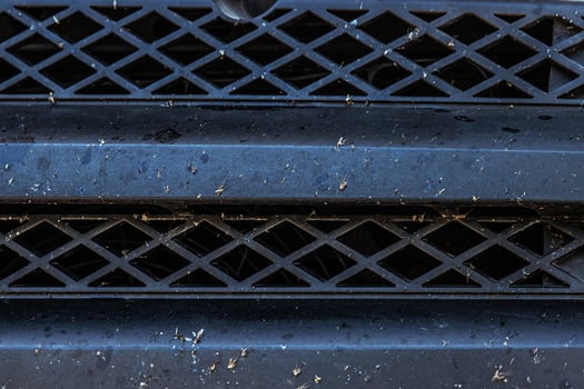 Closeup of a dirty bug splattered vehicle grille with dust and debris. Car front end bumper covered in insects and dirt after a long trip. Auto care, road conditions, air intake system photo