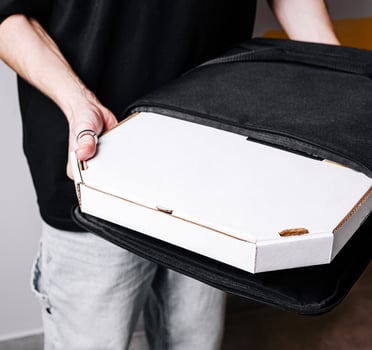 Delivery worker presents a pizza box in a black bag photo