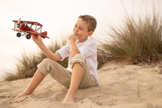 A young boy sits quietly, gazing at an airplane in the sky. His eyes are filled with wonder and curiosity as he watches it soar, lost in thoughts of adventure and dreams of flying photo