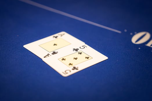 Two playing cards, the 10 of clubs and queen of clubs, rest on a blue poker table with white markings, showcasing a formal gaming setup. photo