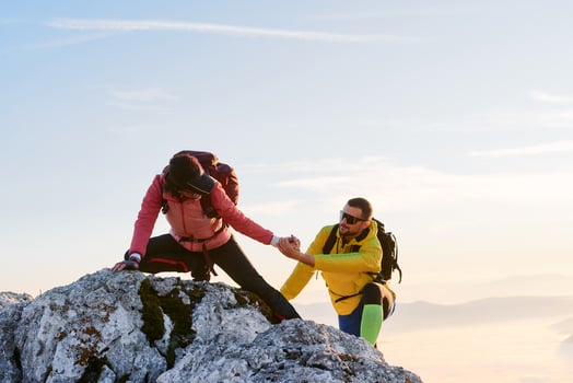 Two hikers, couple in outdoor gear climb rocky terrain with the sun rising behind them.Climbers reaching the mountain peak at sunrise. photo