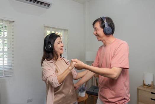 Senior couple smiling and dancing together while enjoying music with headphones at home. photo