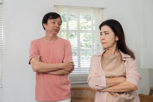 Middle-aged couple standing apart with crossed arms, showing tension indoors. photo