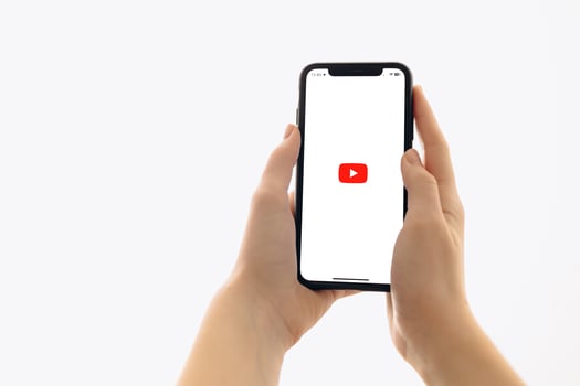 Zaporizhia, Ukraine - January 10, 2025. A woman holds an iPhone with the YouTube app logo on the screen while using a mobile app for business at home. white background photo