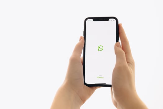 Zaporizhia, Ukraine - January 10, 2025. A woman holds an iPhone with the WhatsApp app logo on the screen while using a mobile app for business at home. white background photo