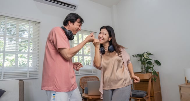Cheerful middle-aged couple playfully dancing and smiling indoors with headphones. photo